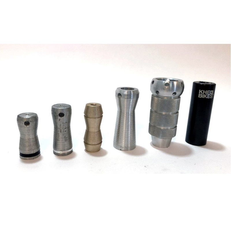 Six BMX axle pegs of different eras and materials lined up side by side, from short aluminum pegs to a taller knurled steel peg to a black plastic peg branded KHE Bikes