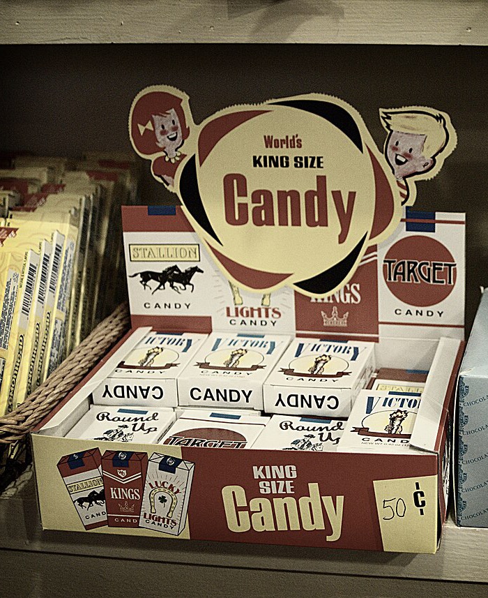 A vintage-style candy shop counter display of candy cigarette packs with brands like Stallion, Kings, Target and Victory
