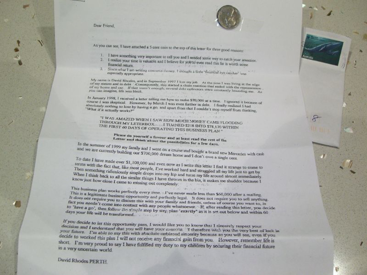 A real chain letter: a typed 'Dear Friend' money-chain letter with a small coin taped to the top and a stamped envelope beside it