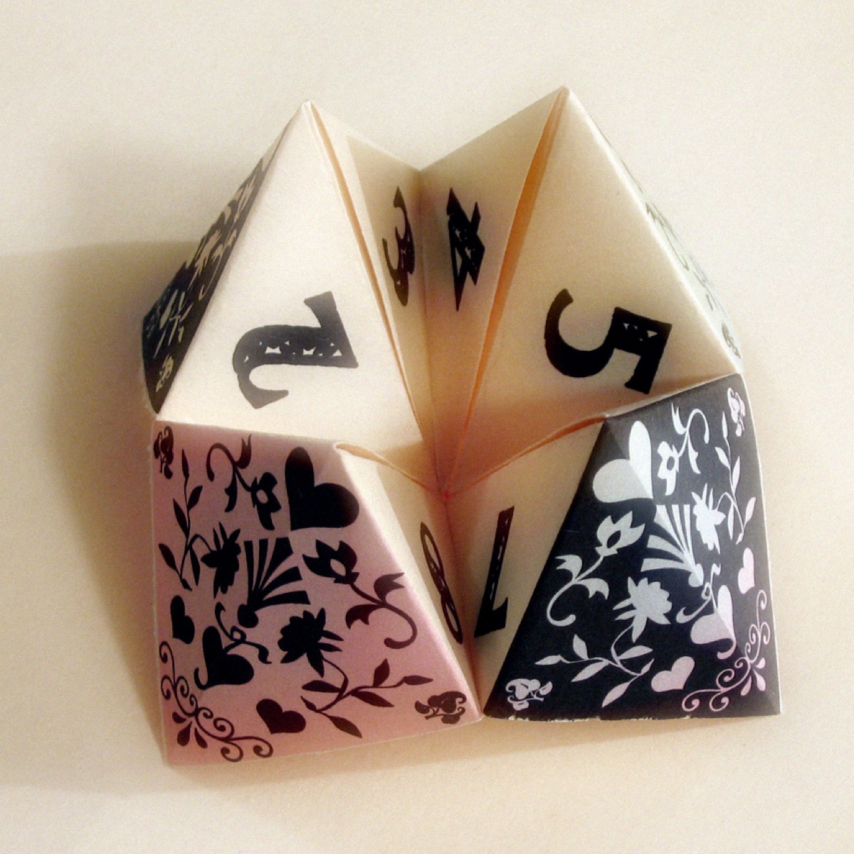 A folded paper fortune teller (cootie catcher), its flaps marked with numbers and patterned in pink and black