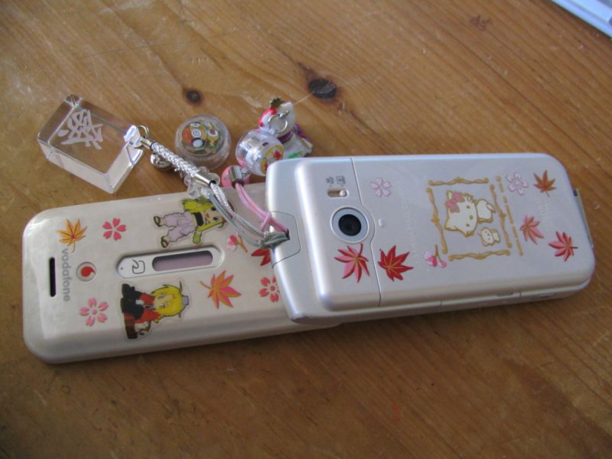 A 2000s flip phone decorated with stickers, with several dangling charms attached to its strap