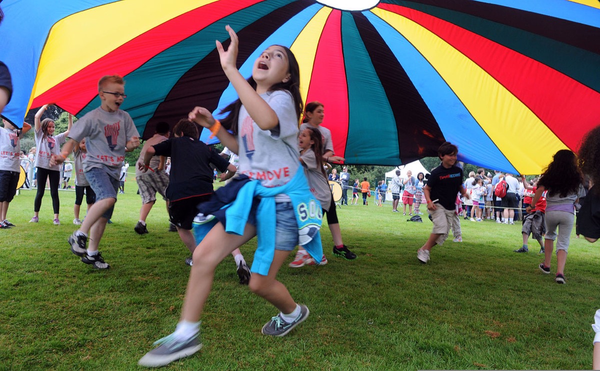 Children running under a giant multicolored play parachute at an outdoor fitness event