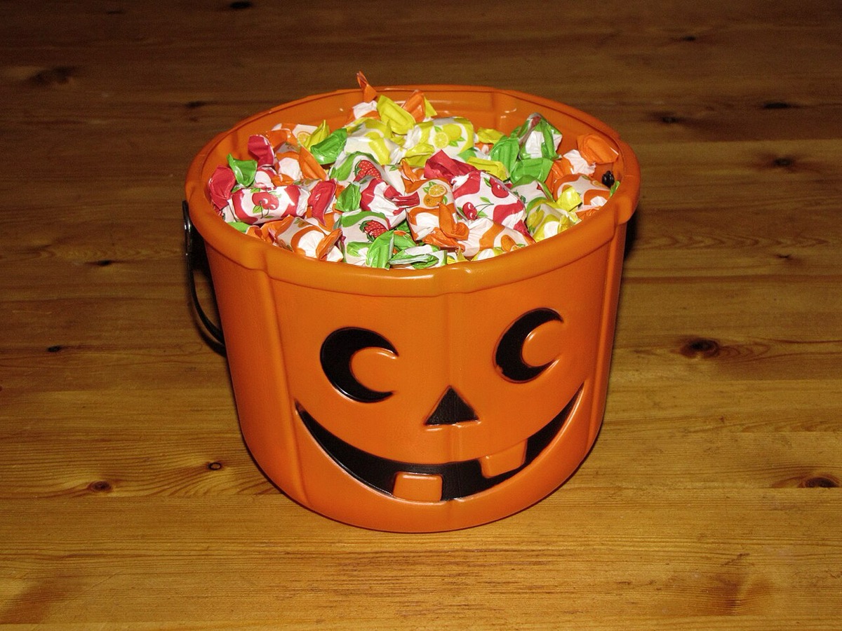 A plastic jack-o'-lantern pail filled to the brim with wrapped candies on a wooden floor