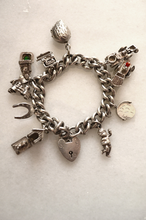 A traditional silver charm bracelet crowded with dangling charms — the older style whose collect-them-one-by-one spirit the flat Italian links reinvented