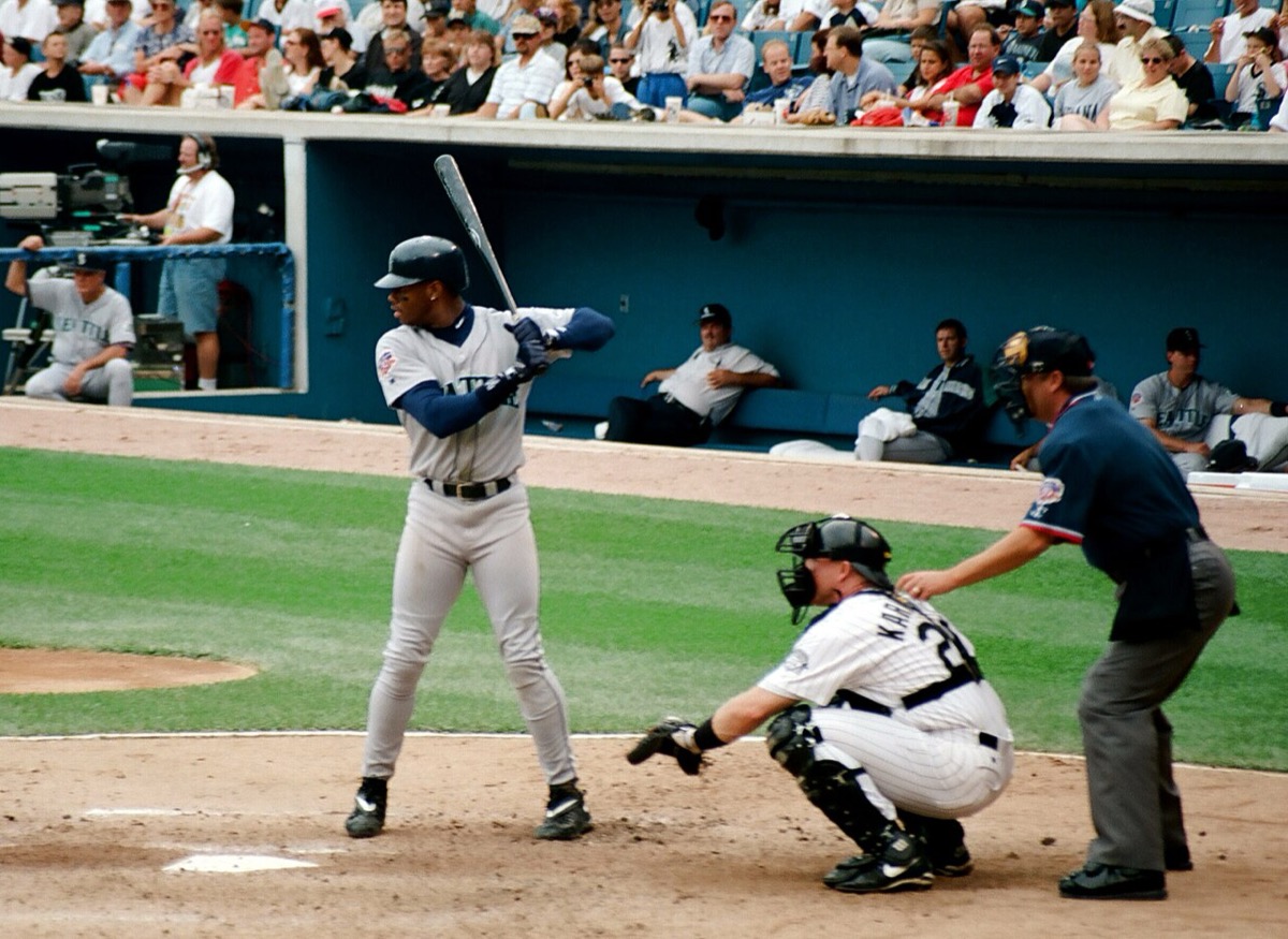 Ken Griffey Jr. at bat in a Seattle Mariners road uniform in 1997, bat cocked, with a catcher and umpire behind the plate