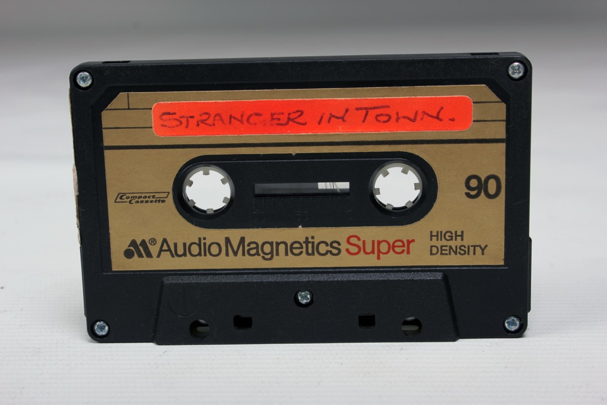 A close-up of a compact cassette with a handwritten label listing the recorded tracks