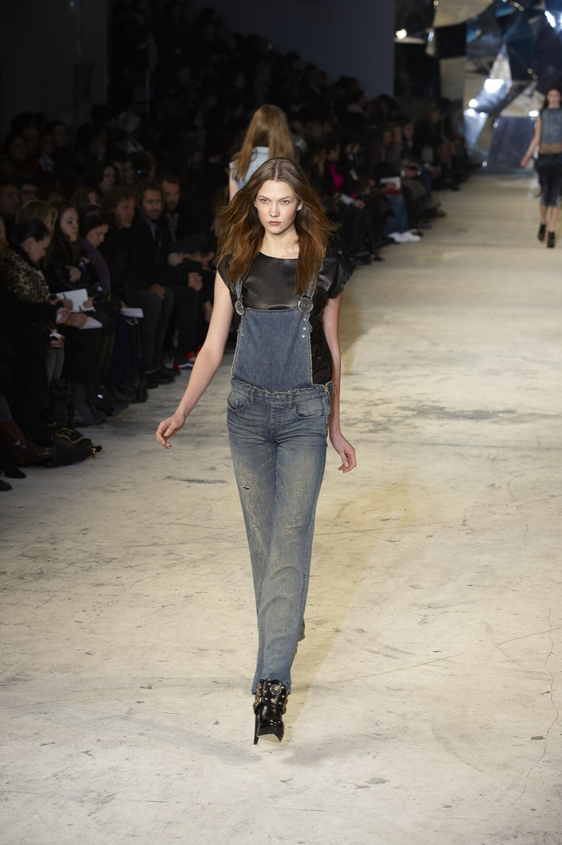A model in faded denim bib overalls at New York Fashion Week, February 2010 — both straps, for the record, buckled.