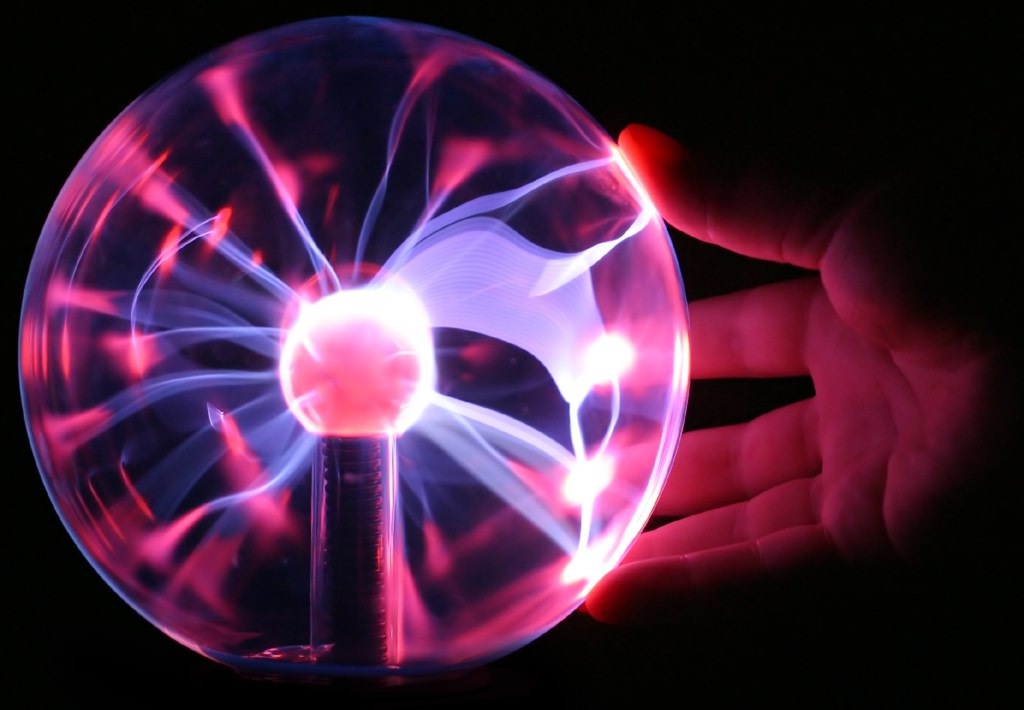 A plasma ball with pink-purple filaments reaching toward a hand touching the glass
