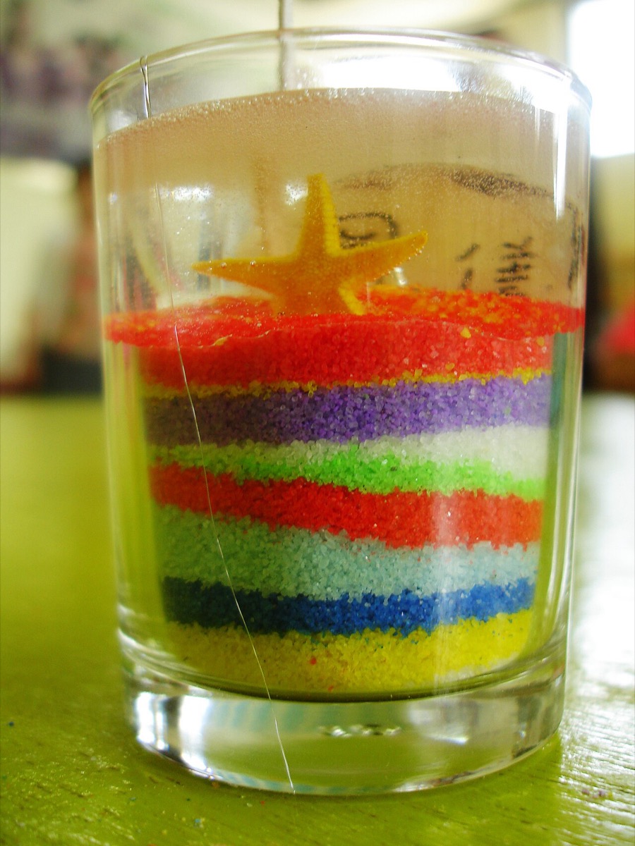 A glass jar of layered rainbow-colored sand topped with a small starfish charm