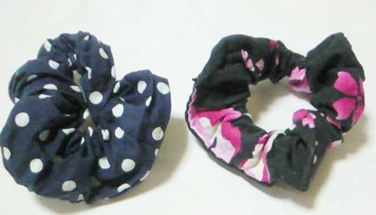 Two fabric scrunchies, one navy polka-dot and one black-and-pink floral print, on a white surface