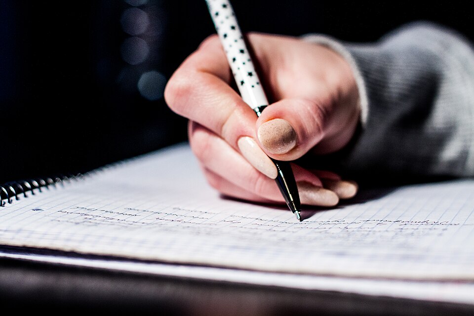 A hand writing with a pen in a spiral-bound notebook — the slam book's native medium
