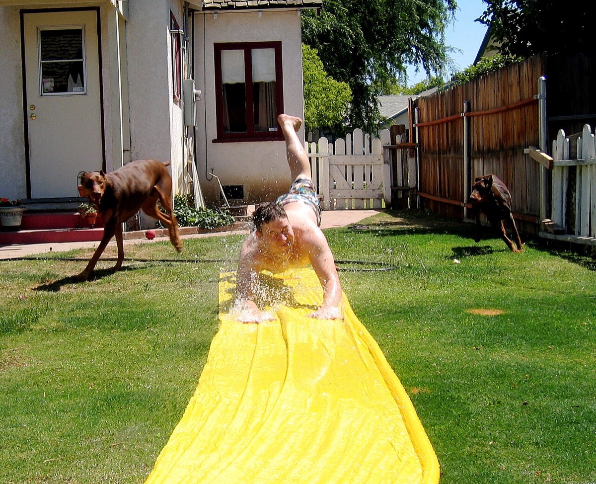 A belly-flop landing on a yellow backyard water slide, mid-splash