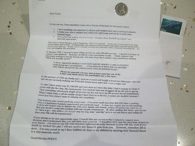 A real chain letter: a typed 'Dear Friend' money-chain letter with a small coin taped to the top and a stamped envelope beside it