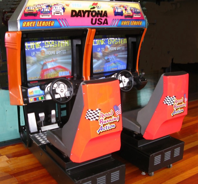 A Daytona USA twin-seat arcade cabinet with its red Road Burning Action seats and Race Leader marquee