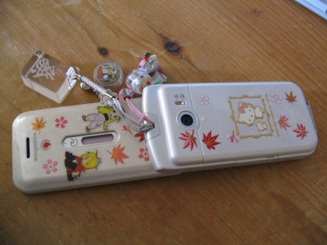 A 2000s flip phone decorated with stickers, with several dangling charms attached to its strap