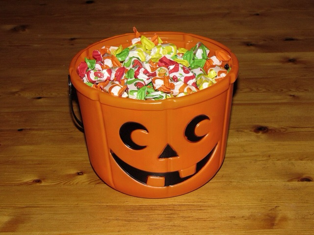A plastic jack-o'-lantern pail filled to the brim with wrapped candies on a wooden floor