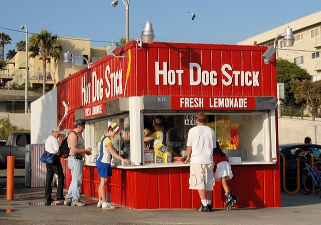 The original red Hot Dog on a Stick stand at Muscle Beach in Santa Monica, with a Hotdogger in the striped uniform at the counter, 2006