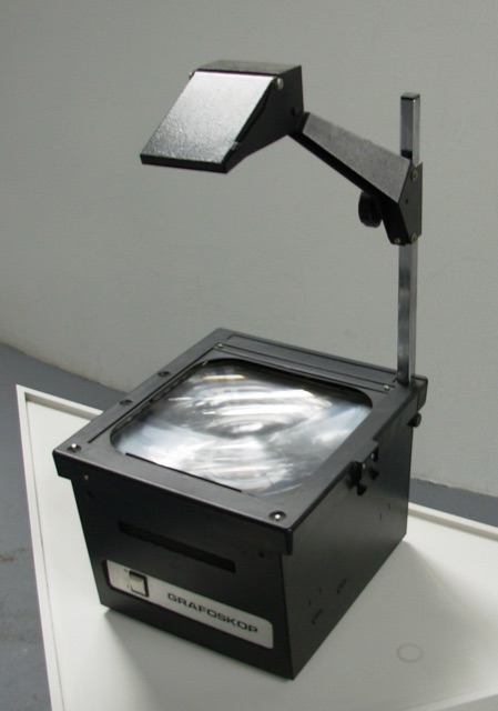A classic overhead projector: black box with glass platen, upright post, and mirror head