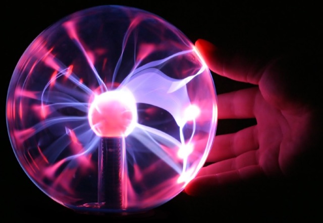 A plasma ball with pink-purple filaments reaching toward a hand touching the glass
