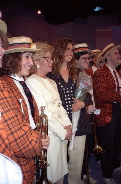 Sally Jessy Raphael in her red-framed glasses on her talk-show set with Brooke Shields and members of the Princeton Band, February 1991