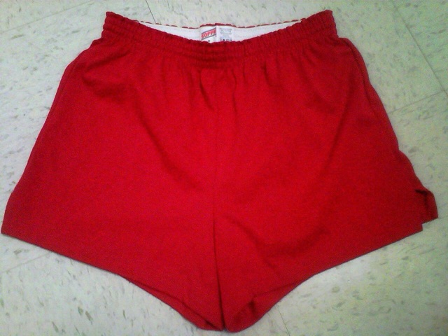 A pair of red Soffe gym shorts laid flat, with the logo waistband showing