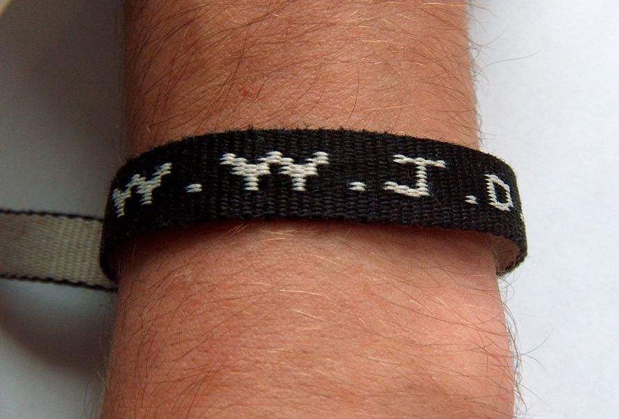 A black woven WWJD bracelet worn on a wrist, with the letters W.W.J.D. stitched in white